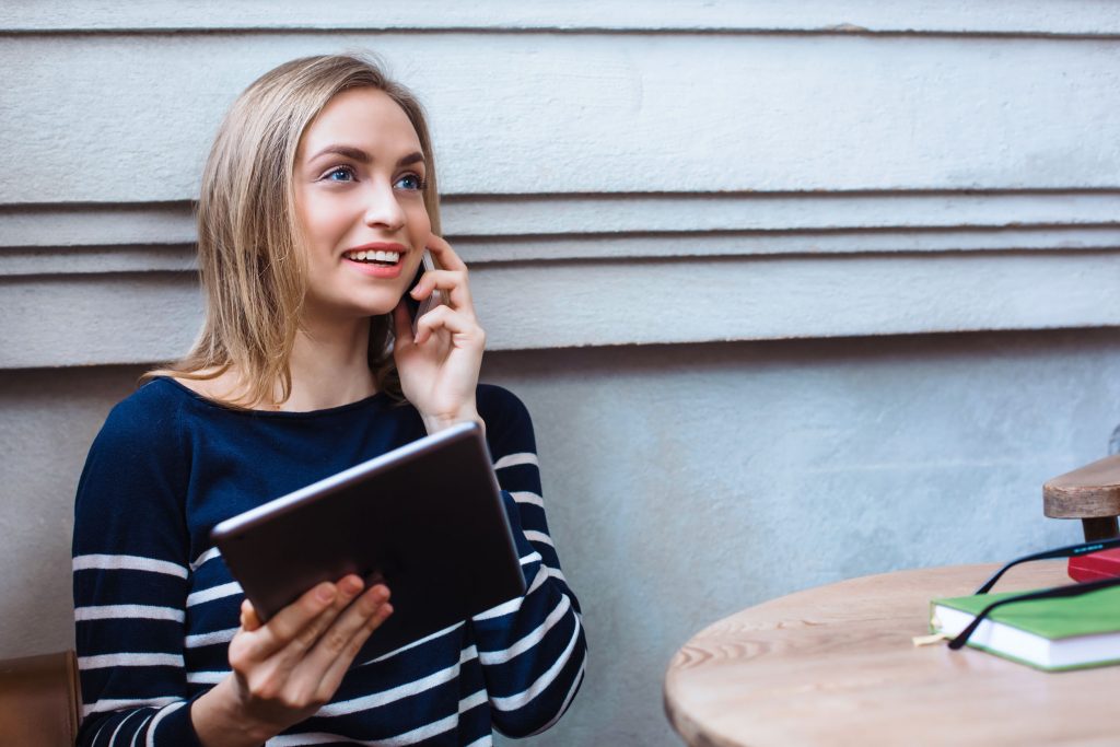 72829564 - young woman talking on the smartphone and smiling. young girl with tablet and cellphone and learns while resting at a cafe. millennials generation y 