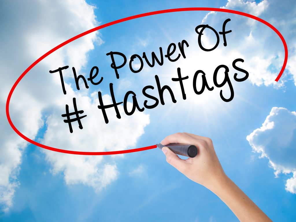 Woman Hand Writing The Power of Hashtags with black marker on visual screen. Isolated on Sunny Sky. Business concept. Stock Photo