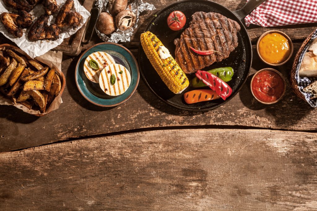 41699431 - high angle view of grilled meal of steak, chicken and vegetables spread out on rustic wooden table at barbeque party