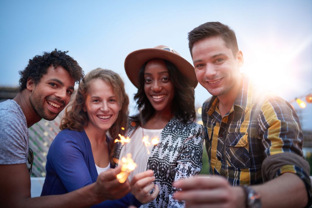 60561627 - four young casual friends having fun with sparkling lights at an urban celebration with a cityscape view in the evening