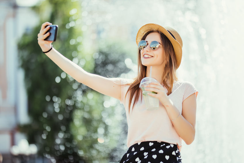 Young girl take selfie from hands with phone on summer city street. Urban life concept.